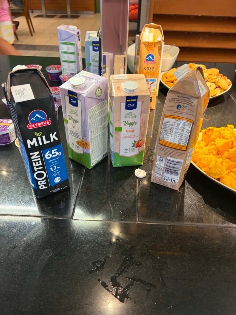 A clear photograph showing a dedicated dietary milk station at the DIT Evrika Beach Club Hotel buffet, featuring plant-based or lactose-free milk options prepared carefully for guests with special dietary needs